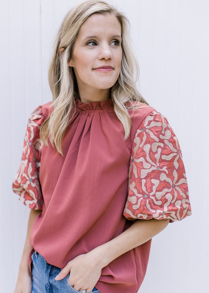 Model wearing a cinnamon top with taupe, cinnamon and green embroidery on bubble short sleeve.
