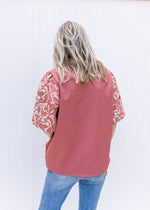Back view of Model wearing a cinnamon top with taupe and green embroidery on bubble short sleeve.
