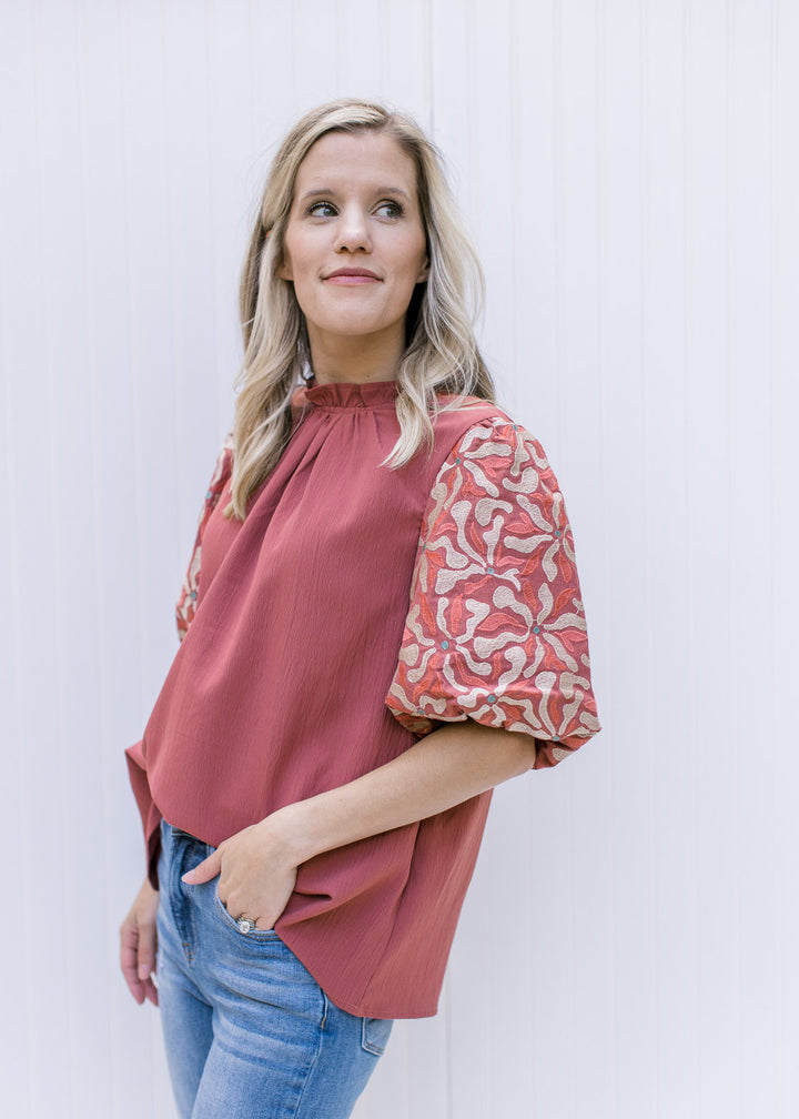 Model wearing jeans with a cinnamon top with taupe and green embroidery on bubble short sleeve.