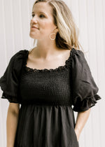 Close up of a smocked bodice and short puff sleeves on model wearing a black midi dress. 