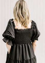 Close up view of smocked bodice and short puff sleeves on a black midi dress with a square neckline.