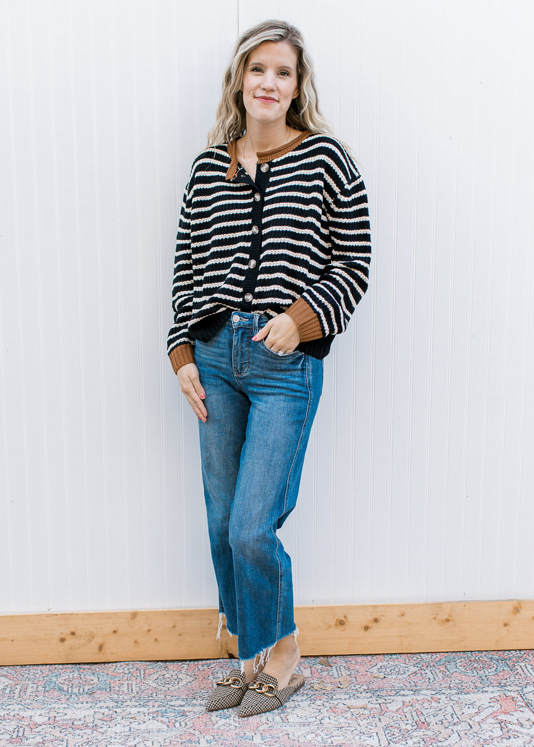 Model wearing jeans and a black cardigan with white stripes and brown detail at neck and cuffs. 