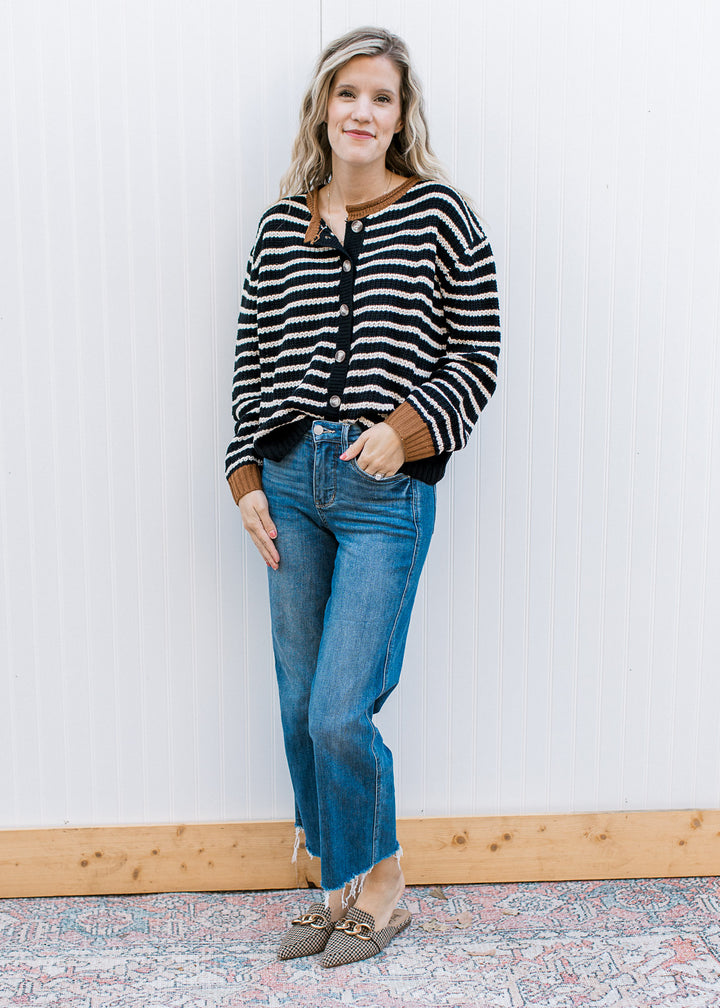 Model wearing jeans and a black cardigan with white stripes and brown detail at neck and cuffs. 