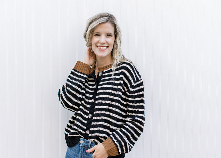 Model wearing a black and white striped cardigan with buttons and brown detail at neck and cuffs. 