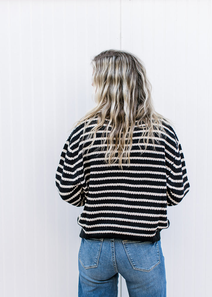Back view of Model wearing a black cardigan with white stripes, buttons and brown details.