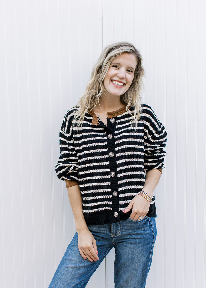 Model wearing a black cardigan with white stripes, buttons and long sleeves pushed up. 