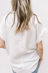 Back view of Model wearing a white button down with patch pockets and cuffed short sleeves.