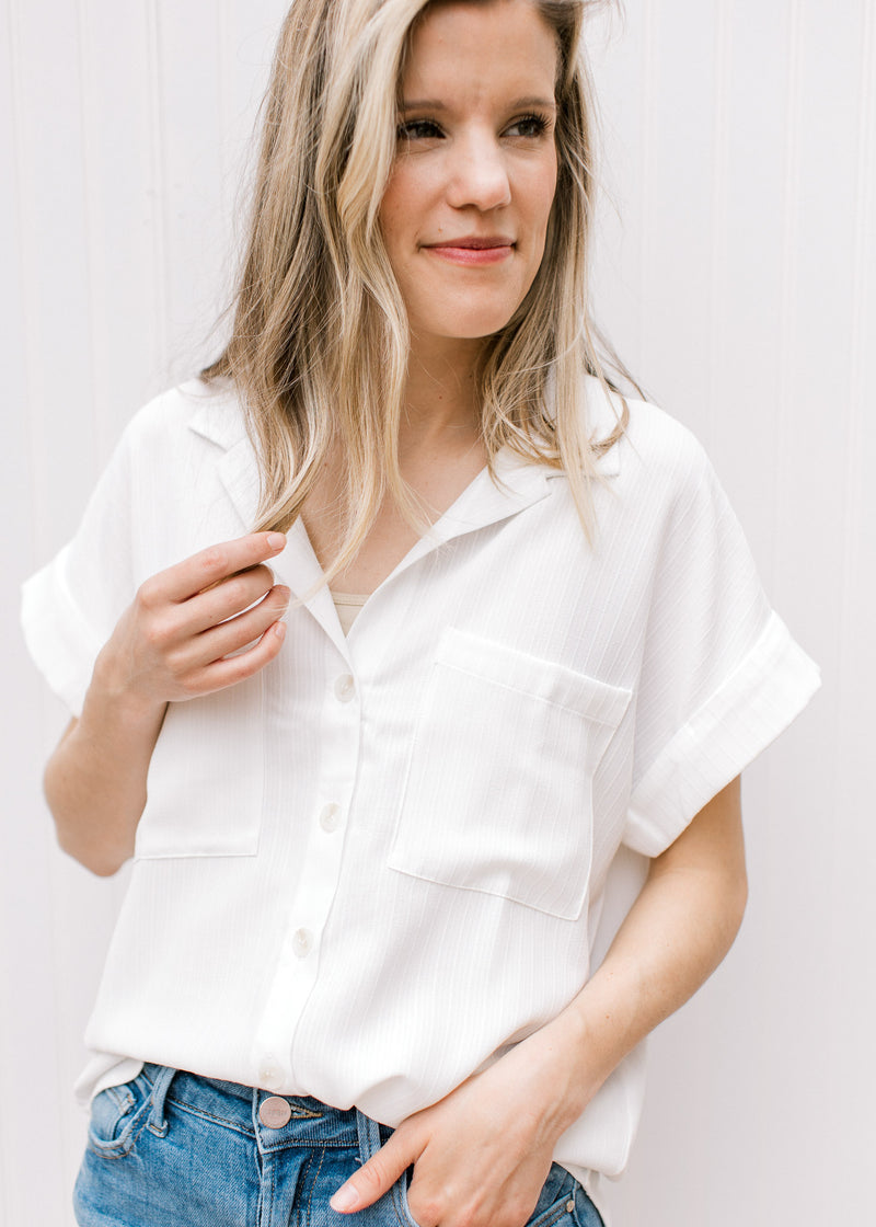 Model wearing a white button down with patch pockets and cuffed short sleeves.