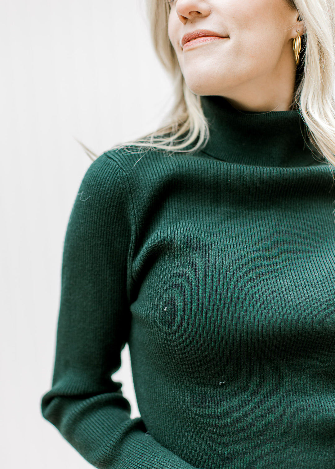 Model wearing a hunter green ribbed top with a turtleneck, long sleeves and a lightweight material. 