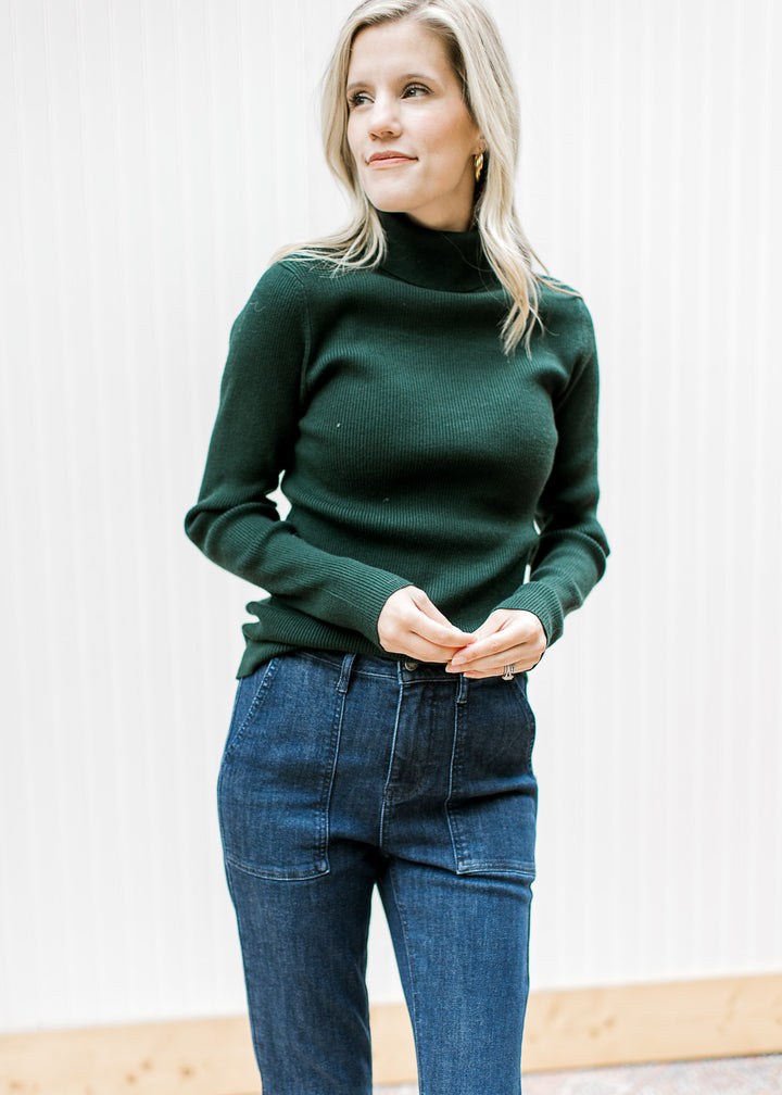 Model wearing jeans and a hunter green ribbed top with a turtleneck and long sleeves. 