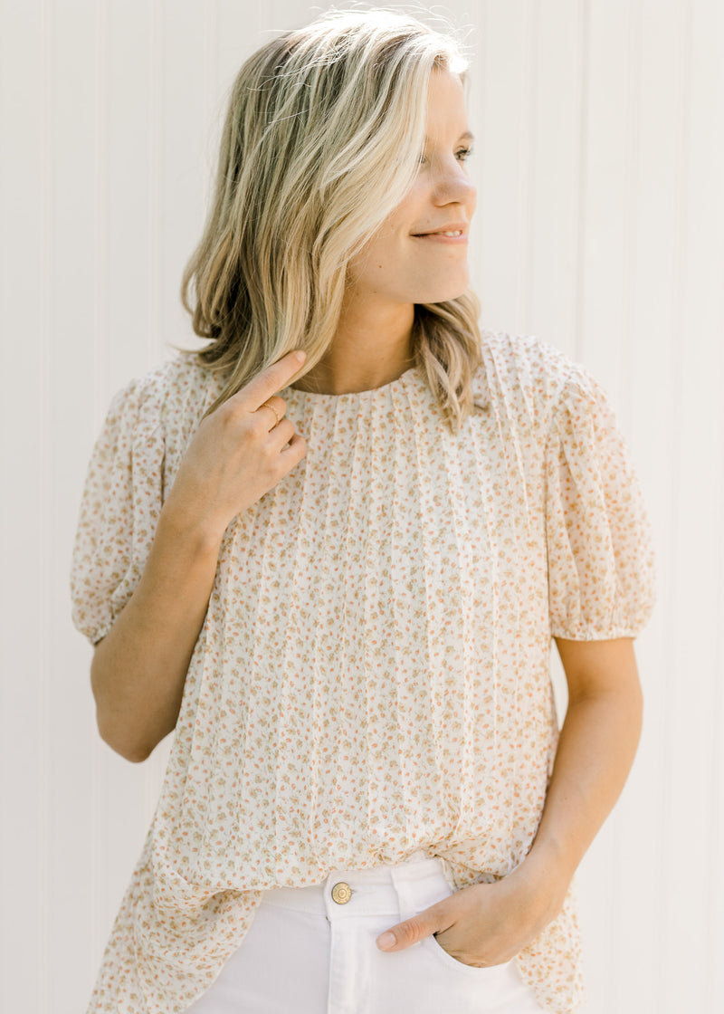 Model wearing a pleated ivory top with a microfloral patter and short sleeves. 