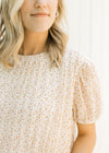 Close up view of Model wearing a pleated ivory top with a microfloral patter and short sleeves. 