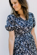 Close up of bubble short sleeves, elastic waist and v-neck on a navy dress with white flowers. 