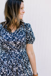 Model wearing a navy a navy v-neck dress with white flowers and bubble short sleeves. 