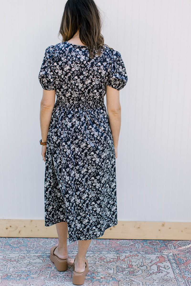 Back view of Model wearing a navy midi with white flowers, elastic waist and bubble short sleeve.