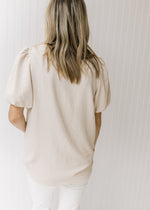 Back view of Model wearing an oatmeal colored v-neck top with short sleeves and a graduated hem.