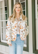 Model wearing a white quilted jacket with fall floral, a flap collar, long sleeves and tie closure.