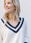 Close up of two navy stripes and ribbing at v-neck of a cream sweater with long sleeves. 