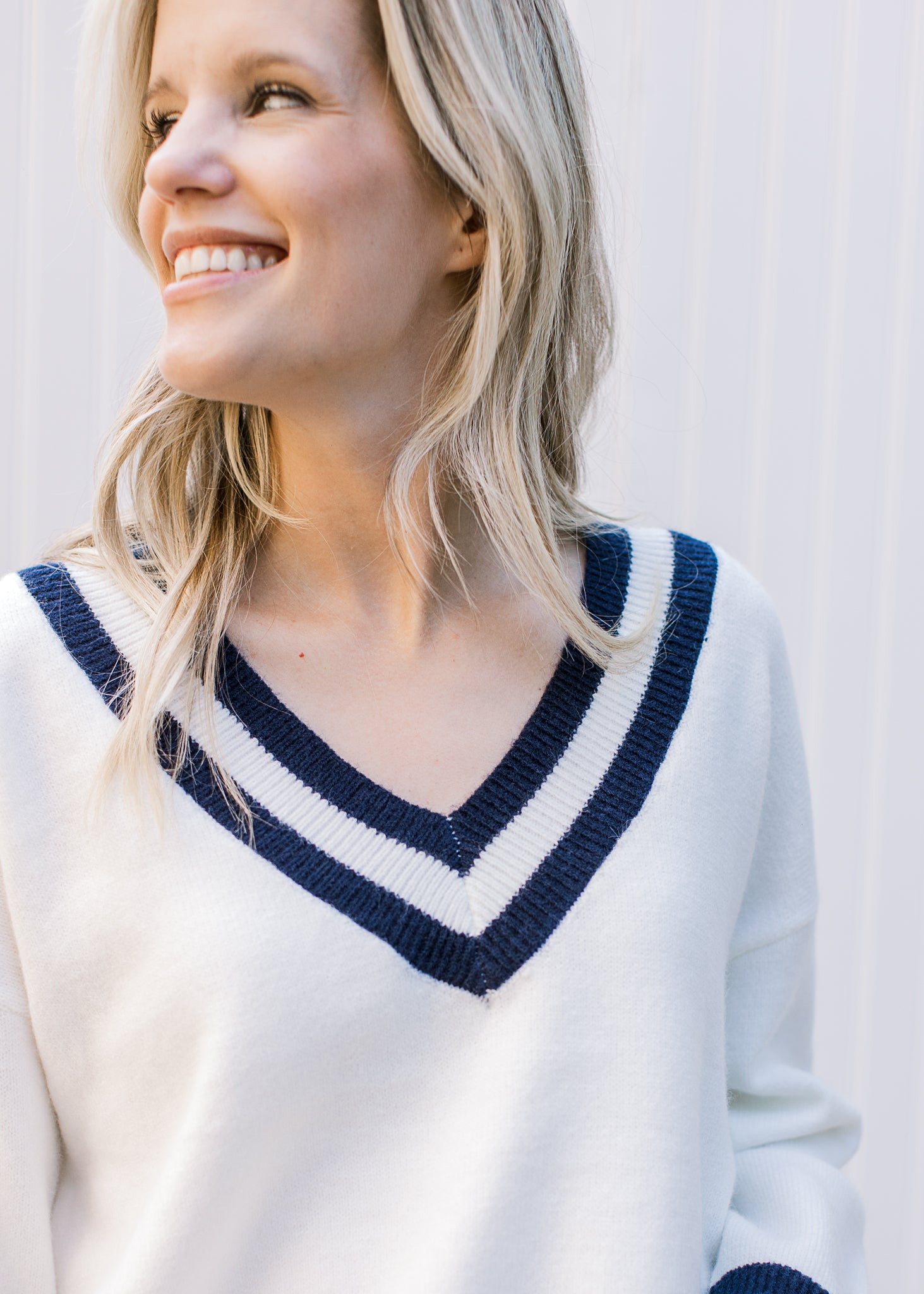 Close up of two navy stripes and ribbing at v-neck of a cream sweater with long sleeves. 