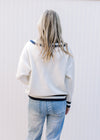 Back view of Model wearing a cream sweater with two navy stripes at neck, hem and cuff. 