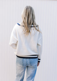 Back view of Model wearing a cream sweater with two navy stripes at neck, hem and cuff. 