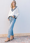 Model wearing a cream v-neck sweater with two navy stripes at neck, hem and cuff. 