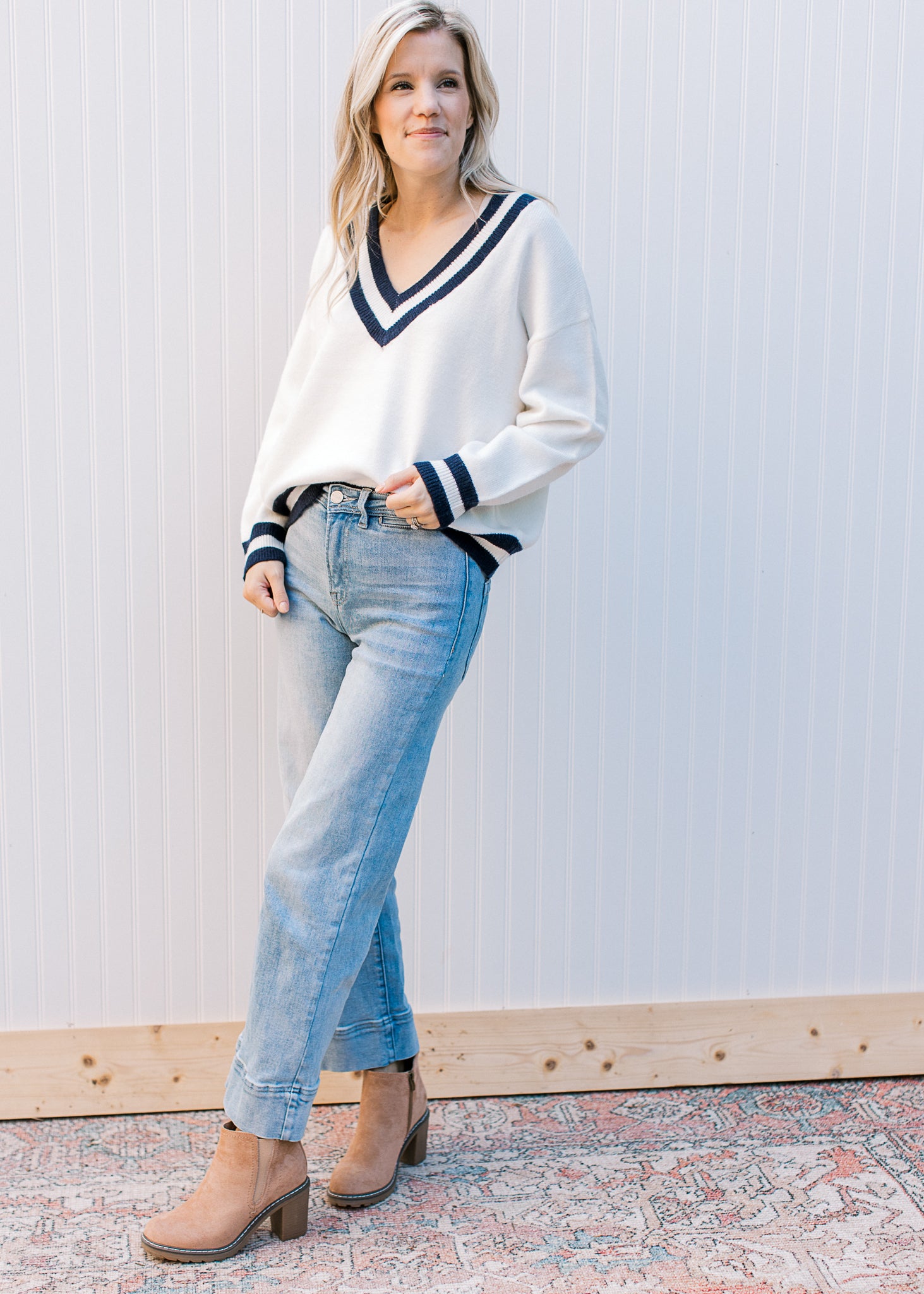 Model wearing a cream v-neck sweater with two navy stripes at neck, hem and cuff. 