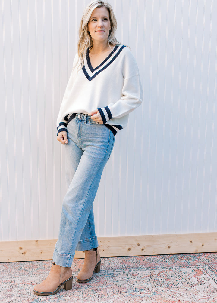 Model wearing a cream v-neck sweater with two navy stripes at neck, hem and cuff. 