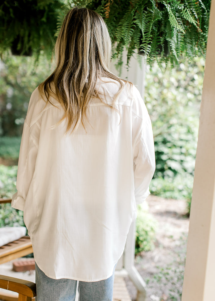 Back view of Model wearing a bright white button up top with double patch pockets and long sleeves. 