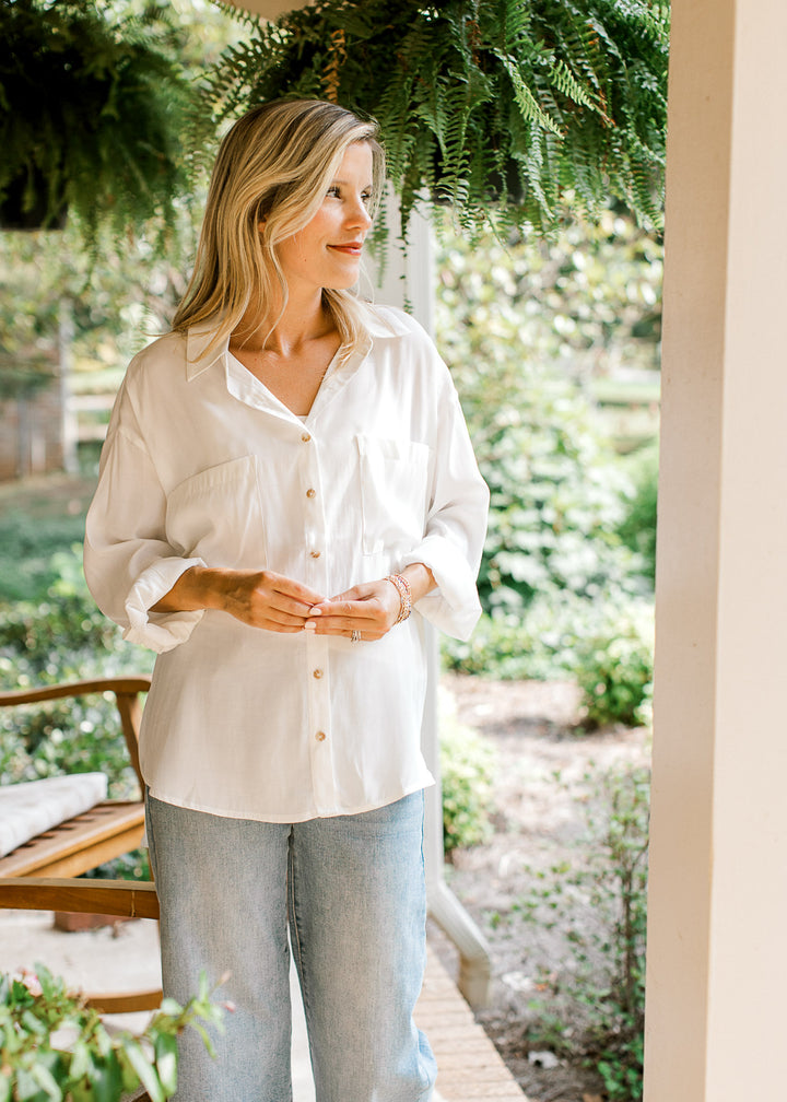 Model wearing jeans and a bright white button up top with double patch pockets and long sleeves. 