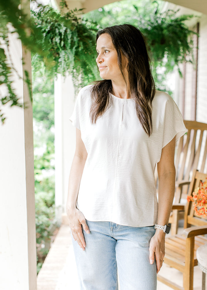 Model wearing a classic white top with a round neck, 2” center seam slit and extended short sleeves.