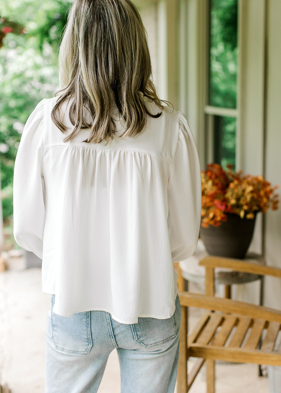 Back view of Model wearing a white blouse with ruffle detail at the neck and front and 3/4 sleeves.