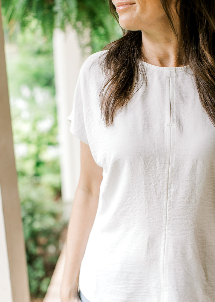 Close up of 2” center slit on a classic white top with extended short sleeves and a round neck.
