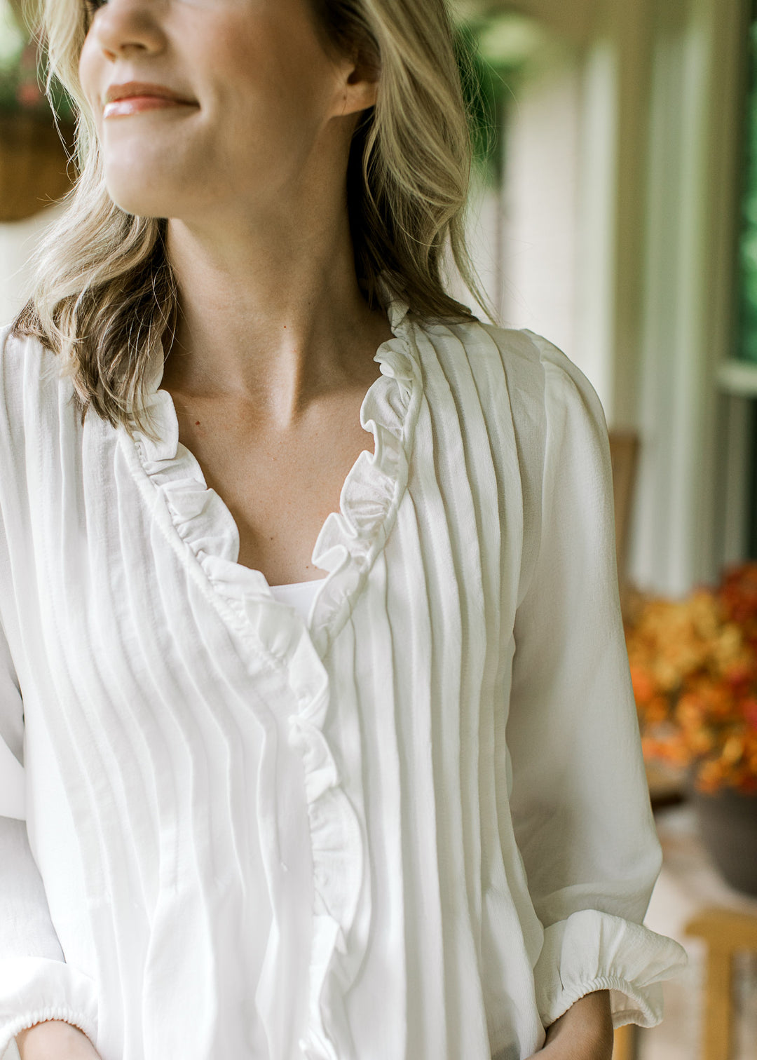 Close up of v-neck with ruffle and pleated front on a white top with 3/4 sleeves with elastic cuff.