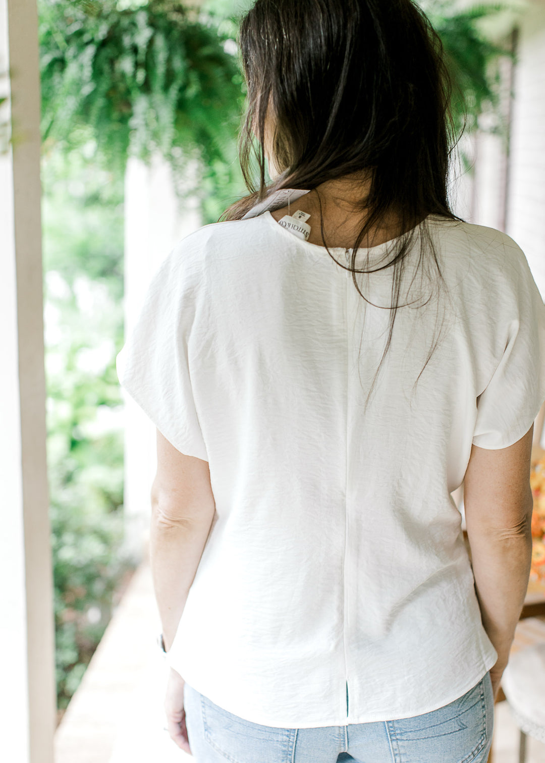 Back view of Model wearing a white top with a round neck, hidden zipper and extended short sleeves.