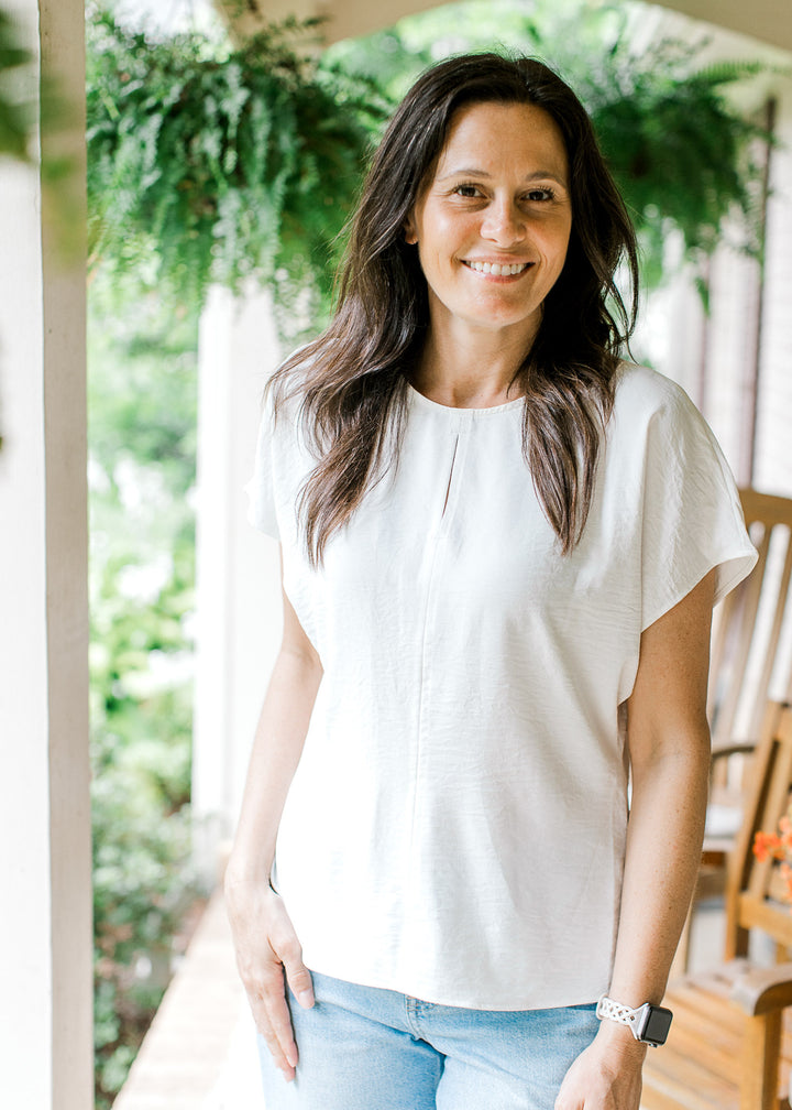 Model wearing a white top with a round neck, 2” center seam slit and extended short sleeves.