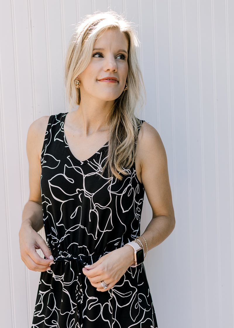 Model wearing a black dress with white flowers and an elastic waist with a tie.