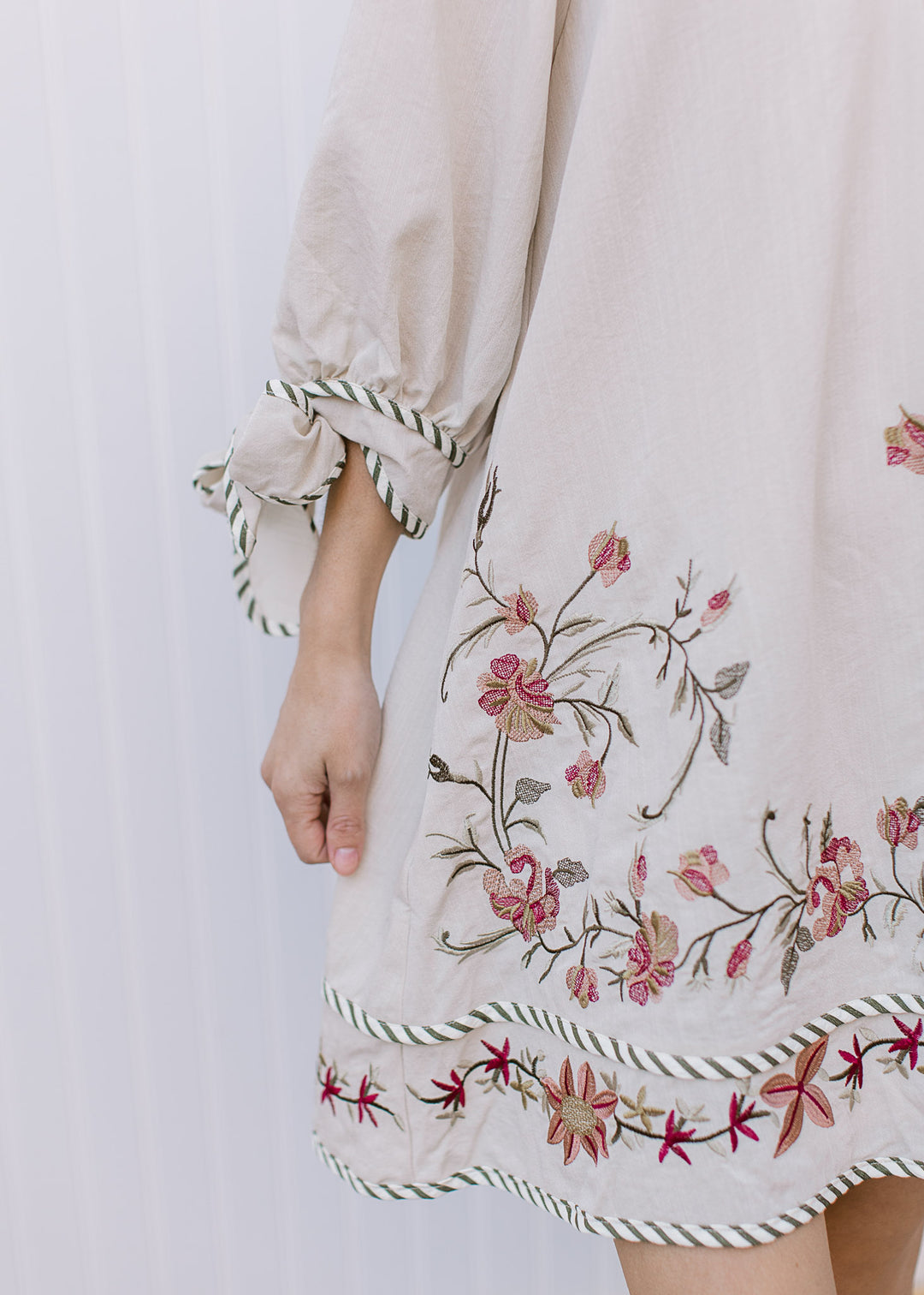 Close up of 3/4 sleeve with tie cuff and green, gold and maroon flowers on a cream dress. 