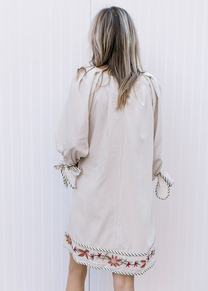 Back view of Model wearing a cream v-neck dress with embroidered flowers and 3/4 sleeves.