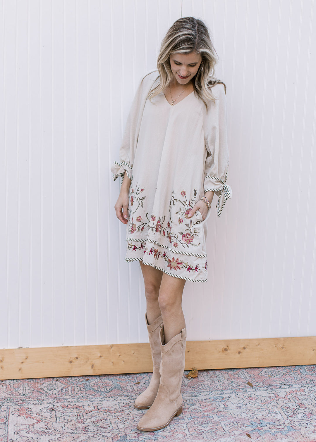 Model wearing boots and a cream v-neck dress with embroidered flowers and 3/4 sleeves.