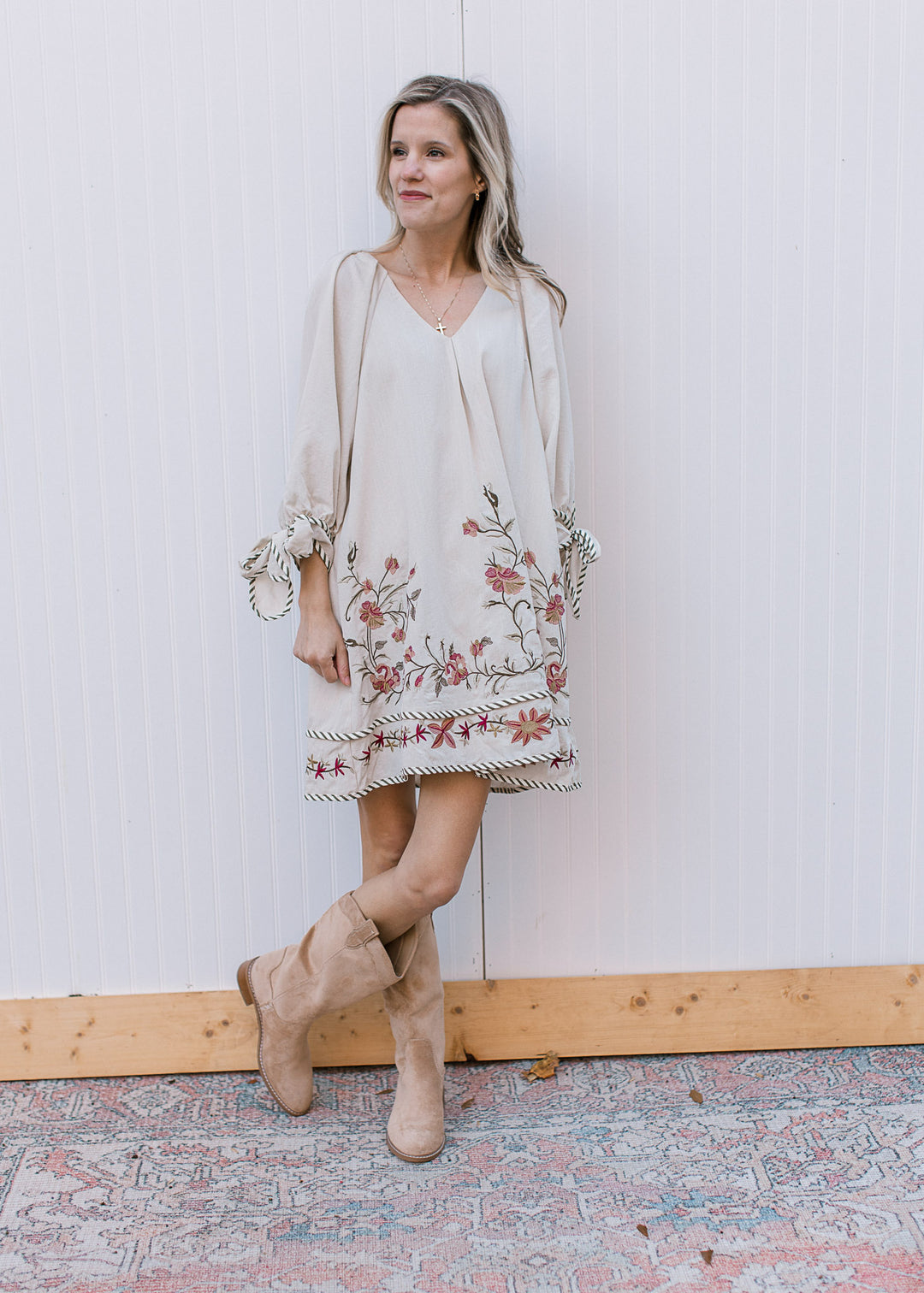 Model wearing a cream above the knee dress with embroidered flowers and 3/4 sleeves.