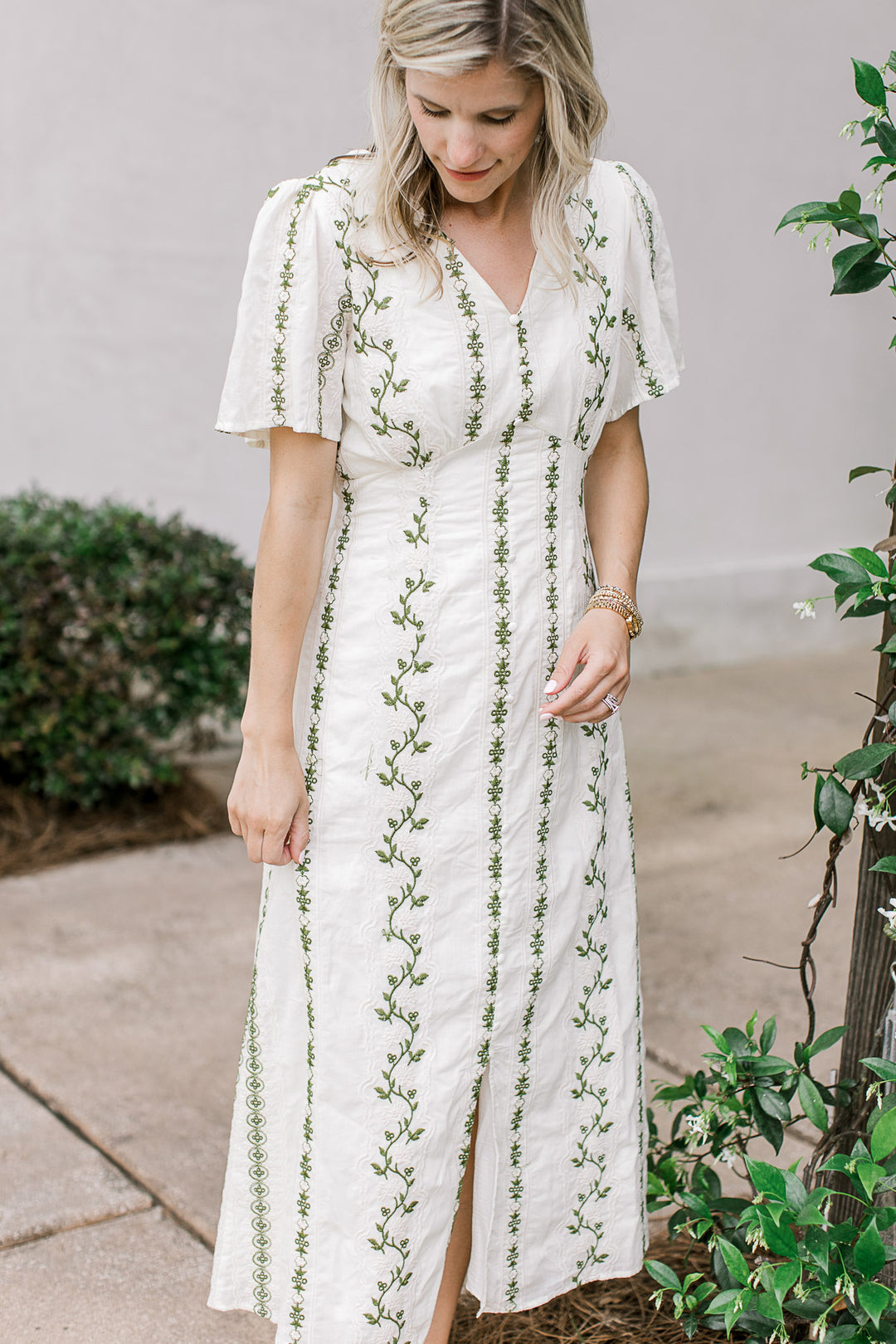 Model wearing a cream midi with olive floral, front slit and short sleeves with pleated shoulders.