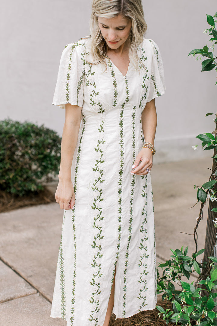 Model wearing a cream midi with olive floral, front slit and short sleeves with pleated shoulders.