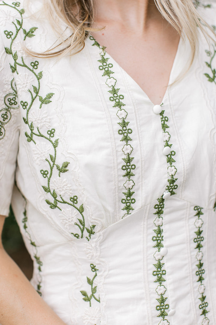 Close up of v-neck and faux buttons on a cream midi with cream and olive embroidered floral. 