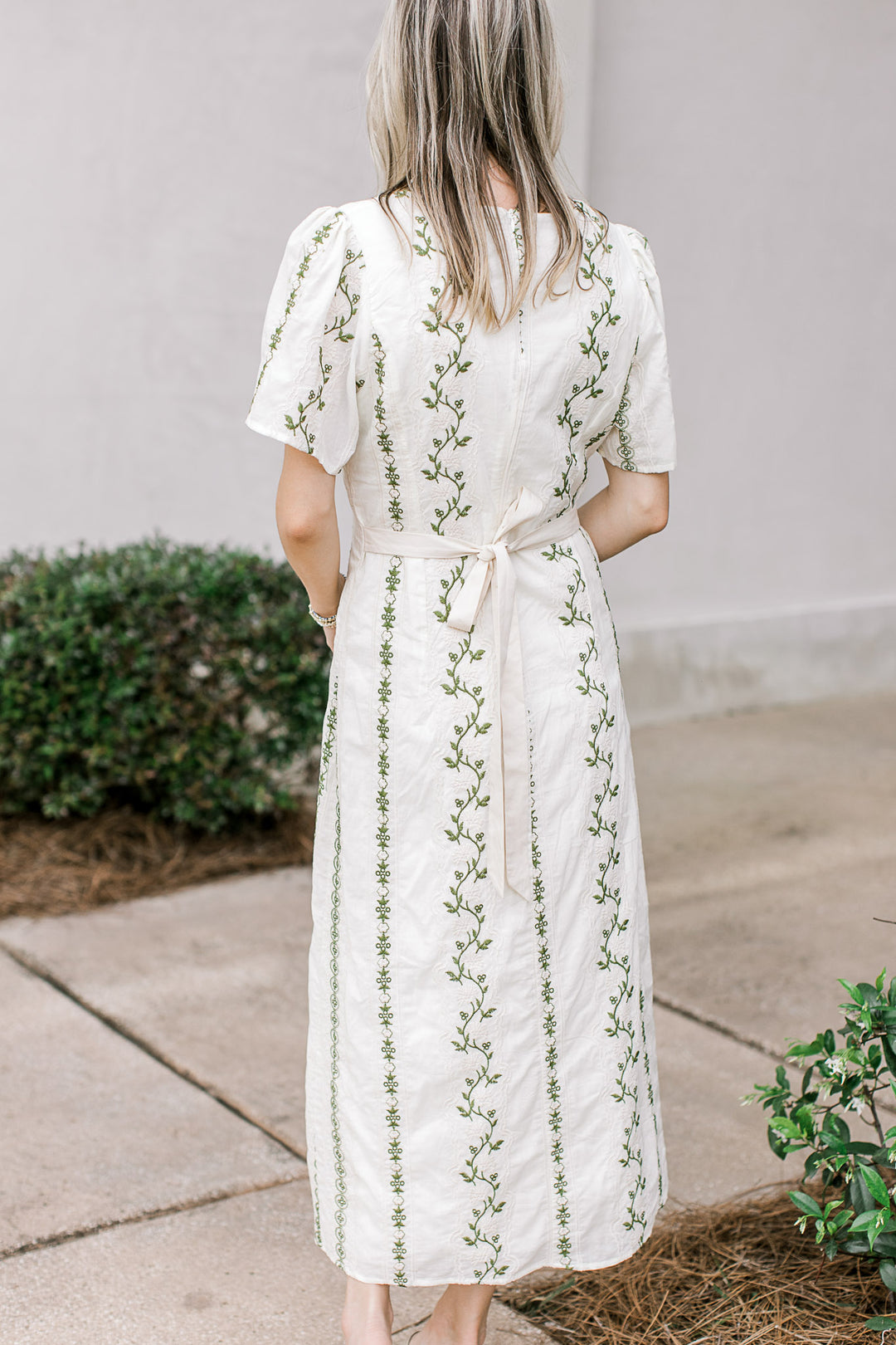 Back view of model in a cream midi with a tie, short sleeves and olive embroidered floral. 