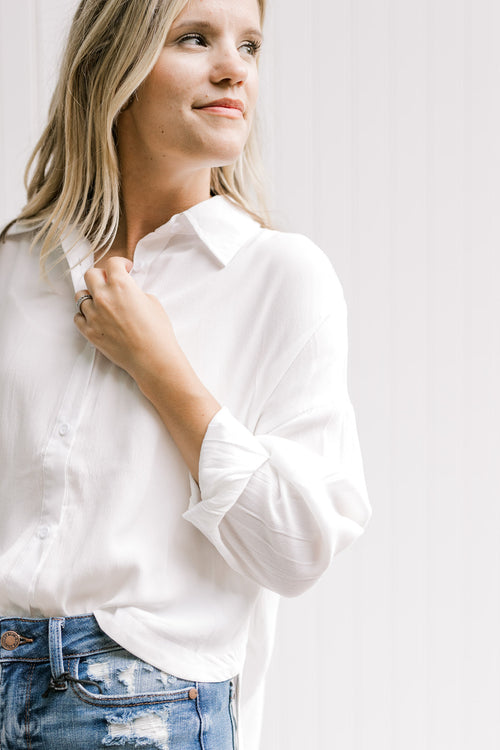 Model wearing a white button down top with a hi-low cut, collar and a polyester material. 