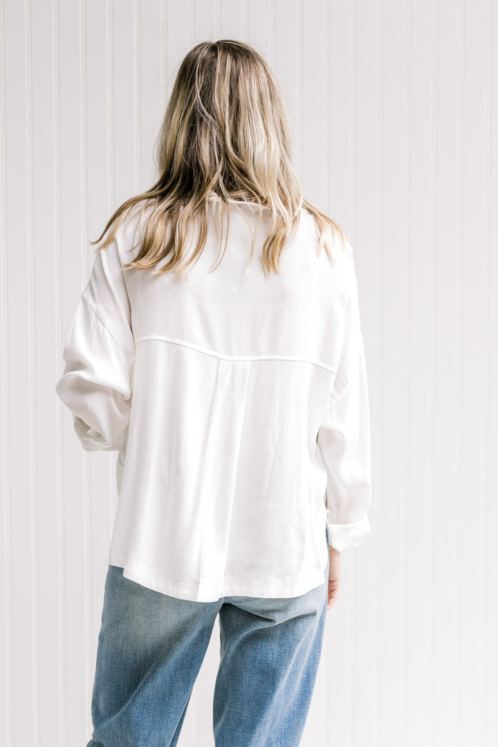 Back view of a Model wearing a white button down top with a hi-low cut and a polyester material.
