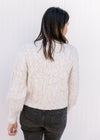 Back view of Model wearing a cream cable knit sweater with long sleeves and mock neck.