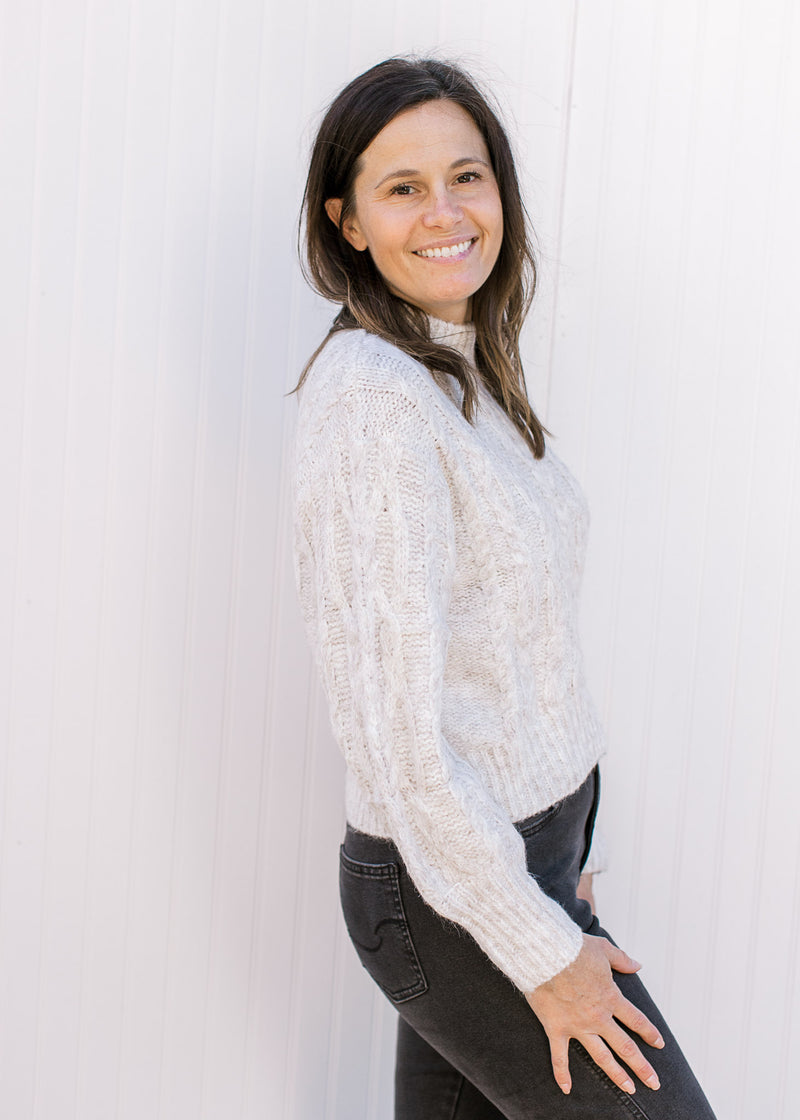 Side view of Model wearing a cream sweater with long sleeves, mock neck and a cropped fit. 