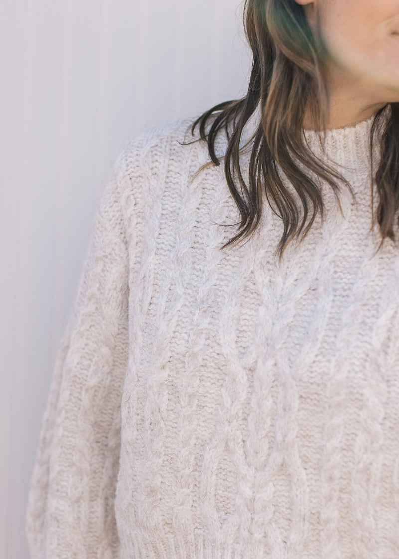 Close up of cable knit and mock neckline on a cream crop fit sweater with long sleeves. 